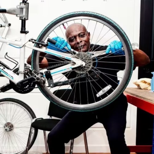 An ex-offender examining the spokes on the rear wheel of a bicycle he has just repaired.